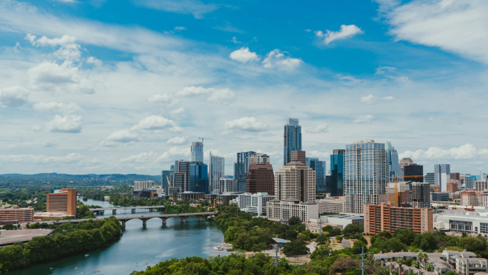 Photo of city skyline with tall buildings, trees, and river.